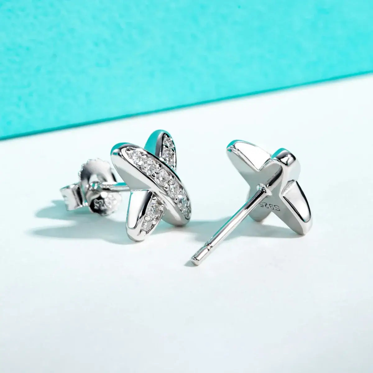 Moissanite diamond stud earrings in 925 sterling silver, featuring a classic cross design on a turquoise background.